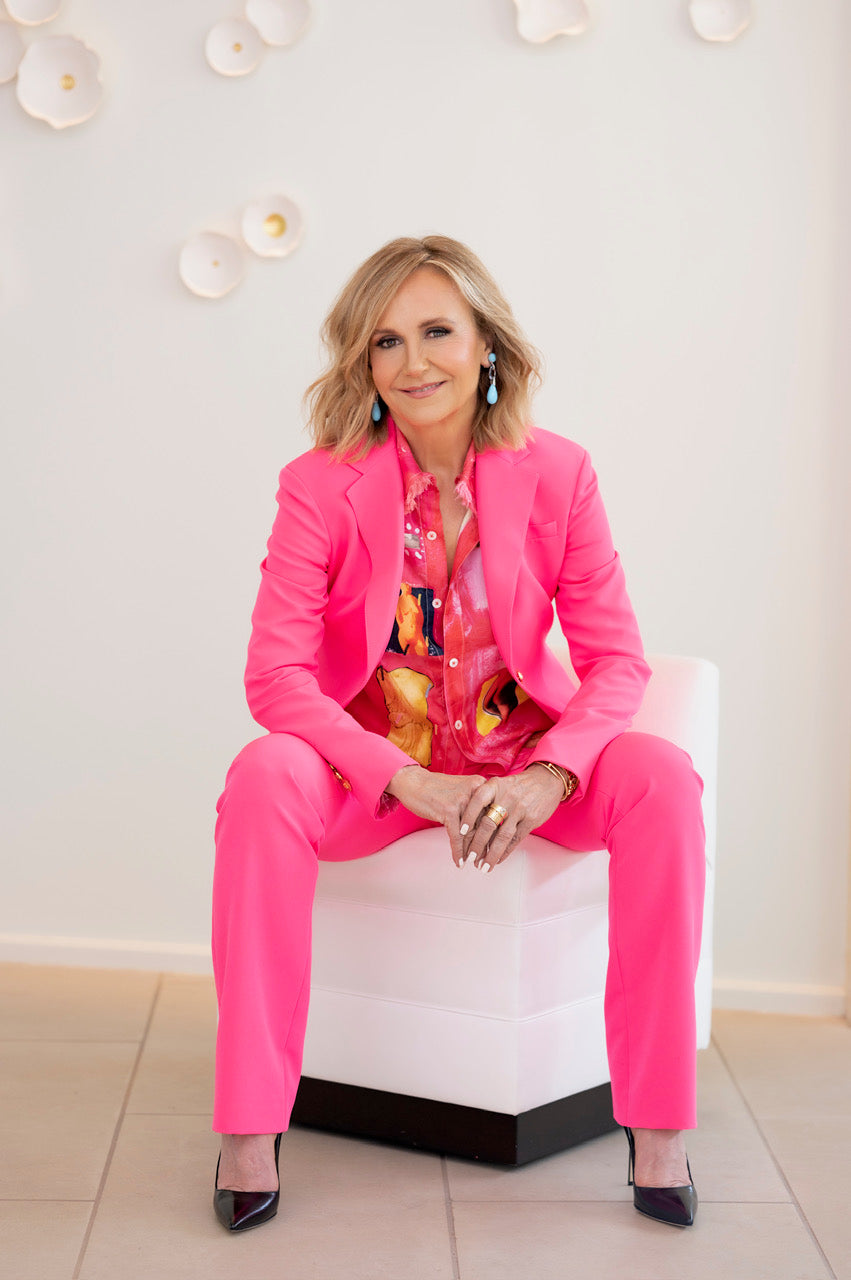 Jane in a bright pink suit sitting on a white chair with a light background